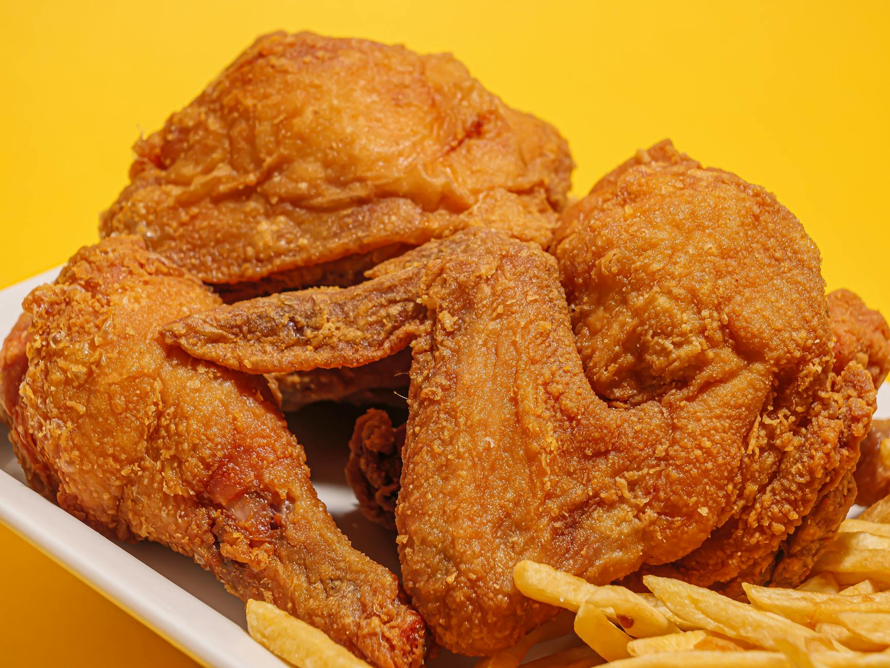 Delicious crispy fried chicken alongside golden French fries on a vibrant yellow backdrop.
